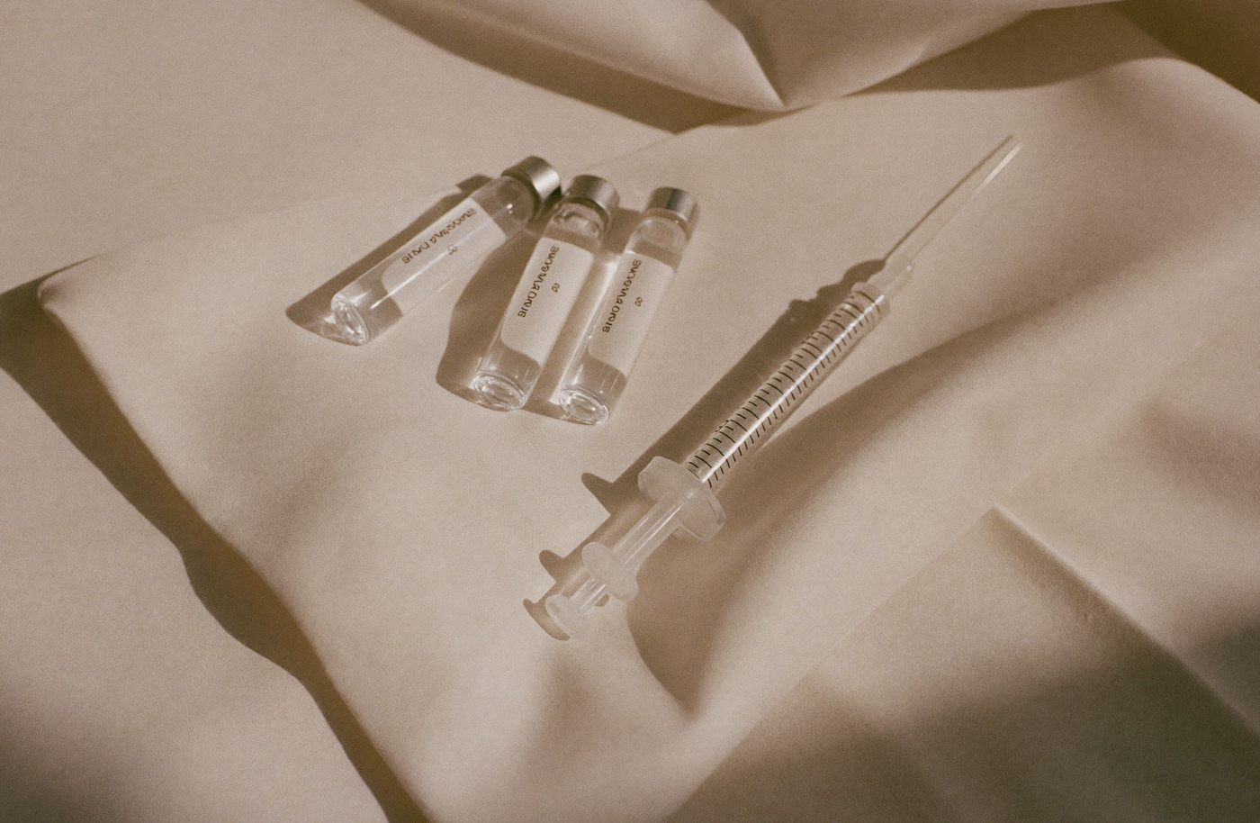 Glass vitamin ampoules and a syringe laid out on cream linen.